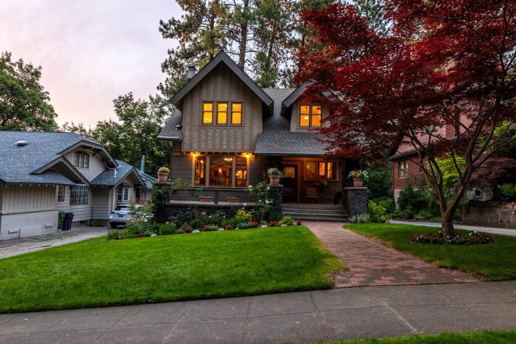 Quaint Victorian-style home with a glowing interior, surrounded by a lush garden at twilight.